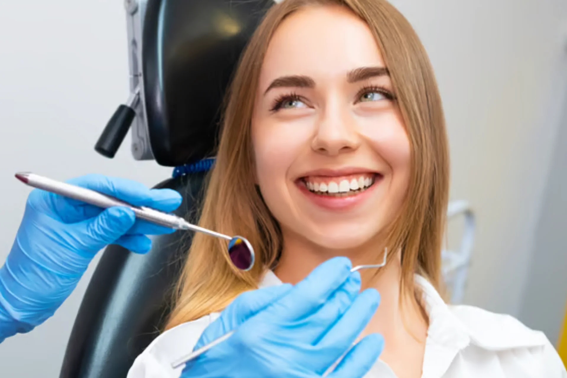 Mujer sonriente en un consultorio dental, recibiendo atención con instrumentos de odontología en manos de un profesional con guantes azules.